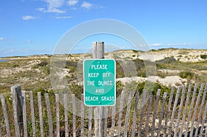 wood fence and sand dunes at the beach with please keep off sign