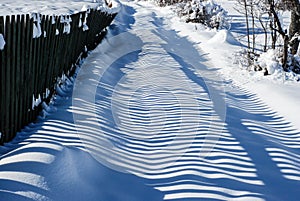 Wood fence shadow in snow. Winter scene in mountains on cold day. Landscape.