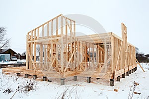 Wood frame house under construction, bare frame with pile foundation, winter season