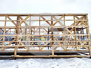 Wood frame house under construction, bare frame, walls with pile foundation, winter season