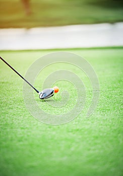 Wood golf club head is about to hit a golf ball on the green grass.