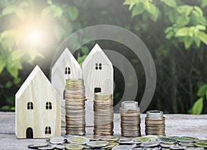 Wood house model with stack of coins on wooden table with green nature blur Background and sunray. Savings Plans for Housing.