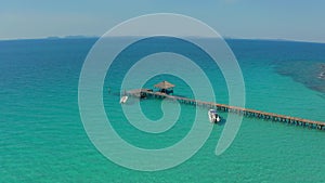 Wood jetty with sailing ship around in the turquoise sea, white beach and forest mountain located in Asia in the open sky day by a