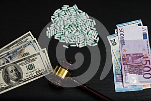 Wood judge`s gavel and scattered colorful drugs on the dollar and euro cash background