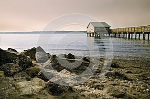 Wood lake pier with a house and a rocky beach