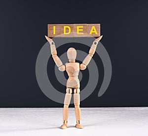 Wood man hold cubes with yellow letters `idea` at the top.