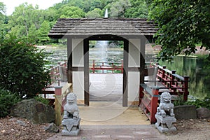 A wood pagoda leading to a viewing platform and seating area over a lake with a water fountain in Janesville, Wisconsin