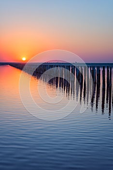 Wood posts for salt extraction in the water of extremely salty lake, amazing nature landscape in sunset light with colored sky