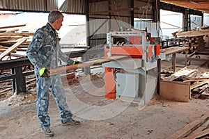 Wood processing at a sawmill. A professional carpenter uses a machine for sawing wooden boards at a sawmill. The concept