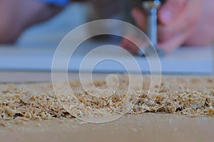 Wood sawdust in carpenter workshop, man drill hole for door hinges in chipboard.