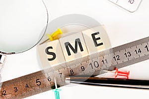 Wood SME on wooden cubes near a measuring ruler, magnifying glass, calculator