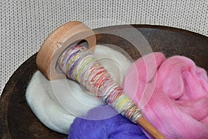 Wood spindle with hand spun yarn in a wood bowl of wool roving