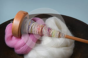 Wood spindle with hand spun yarn in a wood bowl of wool roving