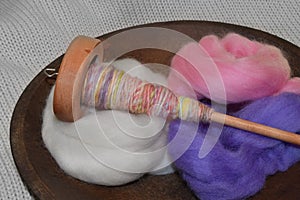 Wood spindle with hand spun yarn in a wood bowl of wool roving