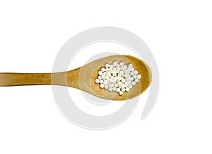 Wood spoon with small white round homeopathy pills isolated on white .