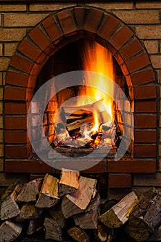 Wood stack and logs burning in brick fireplace