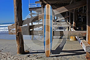 Wood surfboard against California beach pier.