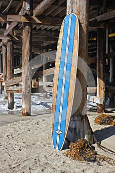 Wood surfboard against California beach pier.