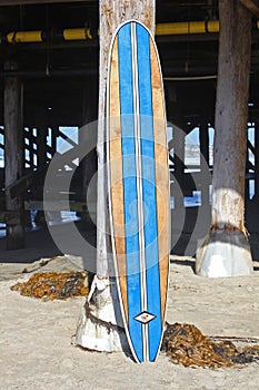 Wood surfboard against California beach pier.