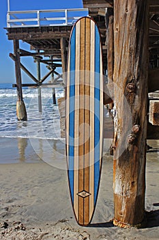 Wood surfboard against California beach pier.