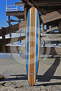 Wood surfboard against California beach pier.