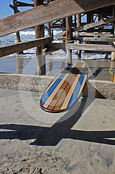 Wood surfboard against California beach pier.