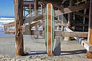 Wood surfboard against California beach pier.