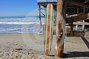 Wood surfboard against California beach pier.