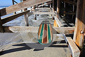 Wood surfboard against California beach pier.