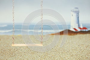 Wood swing on a sandy beach with a lighthouse