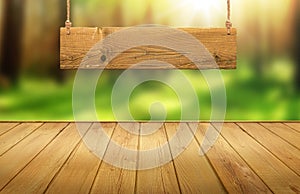 Wood table with hanging wooden sign on green forest blurred background