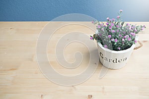 Wood table with pink rose flower on flower pot and concrete wall.