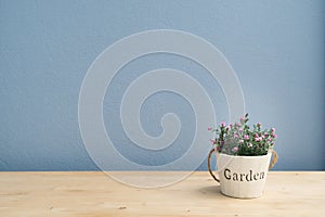 Wood table with pink rose on flower pot and blue cement wall.