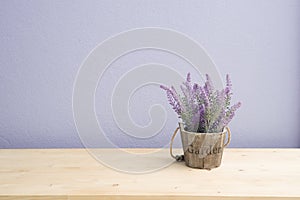 Wood table with purple lavender flower on flower pot and purple cement wall.