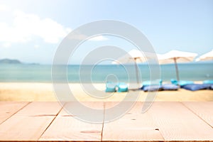 Wood table top on blur beach background with beach bag chairs an