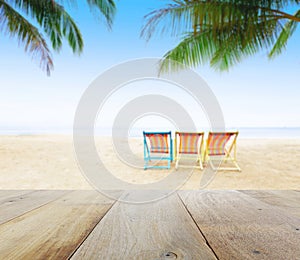 Wood table top on blur beach background with beach chairs under coconut tree