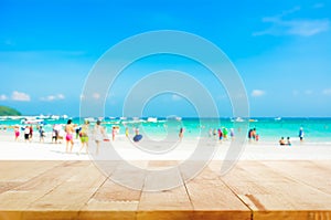 Wood table top on blurred beach background with people in colorful clothes