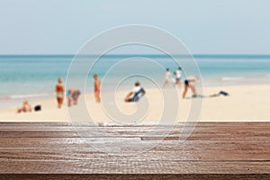 Wood table top on blurred blue sea and white sand beach with some people