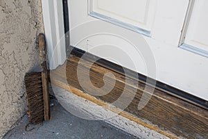 Wood threshold, door and concrete landing of a home with an old shoe brush in corner