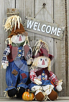 Wood welcome sign hanging on wooden fence by boy and girl scarecrows