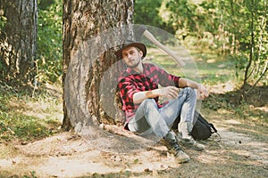 Woodcutter with axe in the summer forest. Illegal logging continues today. Lumberjack standing with axe on forest