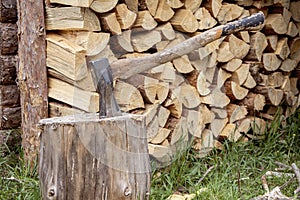 A woodcutter`s metal axe with a wooden handle is stuck in a log for chopping wood against the background of a split tree stacked
