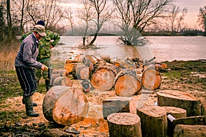 Woodcutter using axe to split large trunk of hardwood, chop firewood at river bank