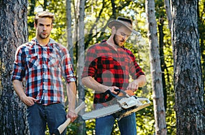 Woodcutters with chainsaw lumberjacks with axe. Hipsters men on serious face with axe. Lumberjack brutal and bearded photo