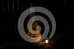 An wooden acoustic guitar is against a grunge textured wall. The room is dark with a spotlight for your copyspace