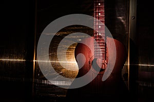 An wooden acoustic guitar is against a grunge textured wall. The room is dark with a spotlight for your copyspace