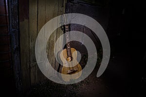 An wooden acoustic guitar is against a grunge textured wall. The room is dark with a spotlight for your copyspace