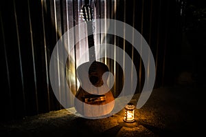 An wooden acoustic guitar is against a grunge textured wall. The room is dark with a spotlight for your copyspace