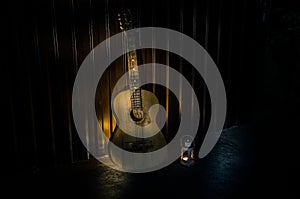 An wooden acoustic guitar is against a grunge textured wall. The room is dark with a spotlight for your copyspace