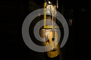 An wooden acoustic guitar is against a grunge textured wall. The room is dark with a spotlight for your copyspace